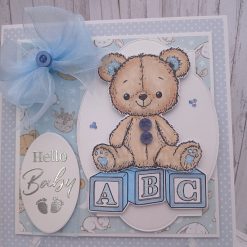 Hello Baby - Teddy bear perched on three pastel blue alphabet blocks